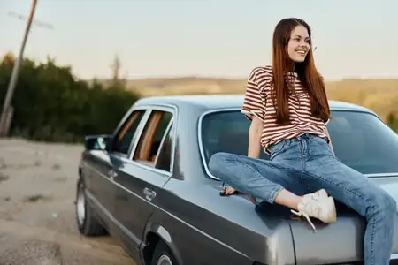 Молодая женщина сидит на багажнике автомобиля и отдыхает после трудной дороги, любуясь природой с красивым видом