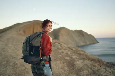 Красивая путешественница стоит у моря в горах, на заднем плане закат, кадр обрезан