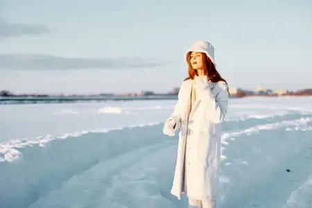 Молодая женщина улыбается, прогуливаясь в зимнем настроении в белом пальто, наслаждаясь свежим воздухом
