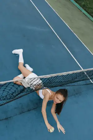 Спортивная молодая женщина в спортивной одежде демонстрирует свою преданность теннису, пытаясь поймать мяч на ярком синем корте, воплощая силу и спортивный дух