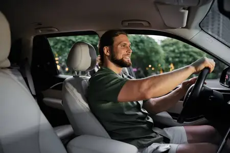 Счастливый мужчина наслаждается поездкой в просторном автомобиле в окружении яркого городского пейзажа и зелени