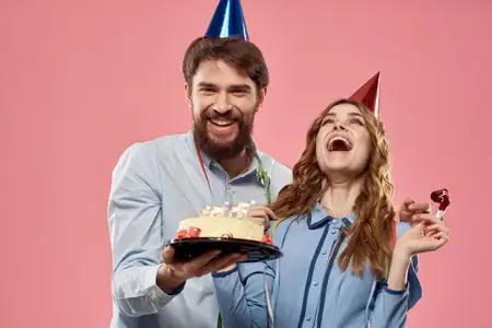 Мужчина и женщина на вечеринке, корпоратив, розовый фон, веселье, торт, колпак