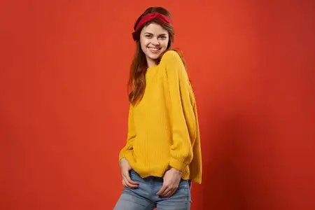 Привлекательная женщина в жёлтом свитере, модная одежда, уличный стиль, красный фон