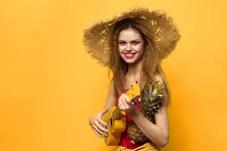 Женщина держит укулеле и соломенную шляпу на экзотическом жёлтом фоне