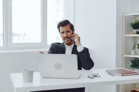 Мужчина в белом костюме, счастливый, улыбается, работая за компьютером