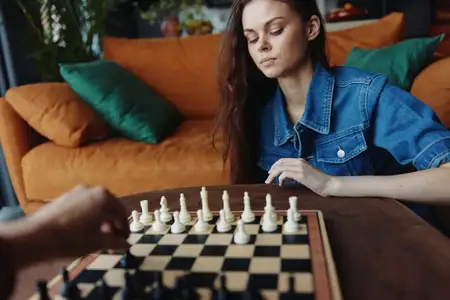 Молодая женщина играет в шахматы за столом перед диваном в гостиной с элегантным интерьером