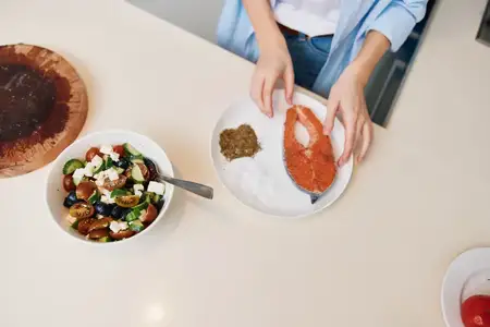 Женщина готовит вкусное домашнее блюдо, используя различные ингредиенты на кухонной стойке, рядом стоят миска и тарелка с едой