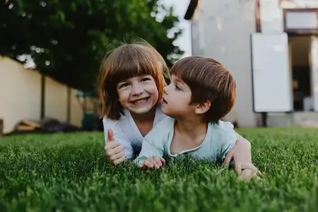Двое весёлых детей лежат на траве, игриво взаимодействуя друг с другом