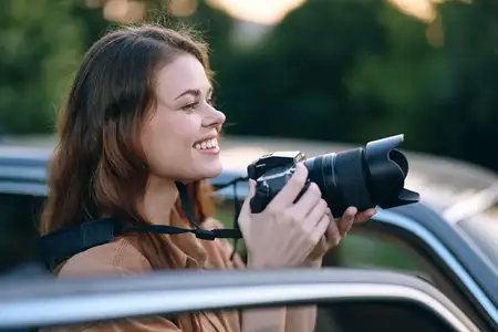 Счастливая молодая женщина с зеркальной фотокамерой улыбается, фотографируя на открытом воздухе, олицетворяя страсть, креативность и радость от съемки моментов