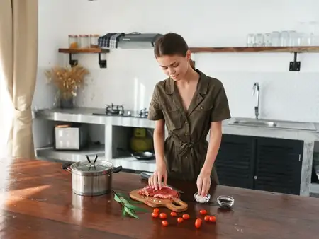 Женщина на кухне готовит обед из мяса, овощей и специй на деревянном столе на фоне стильной кухни