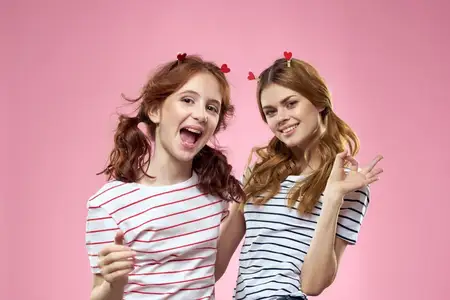 Счастливые сёстры веселятся на розовом фоне, а на головах у них прищепки в форме сердечек