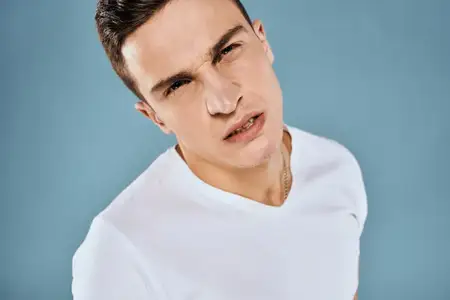 Эмоциональный недовольный мужчина, кадрированный вид, в белой футболке на синем фоне