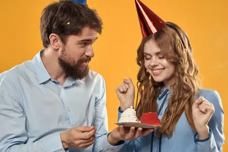 Мужчина и женщина веселятся на праздновании дня рождения на жёлтом фоне, на них праздничные колпаки