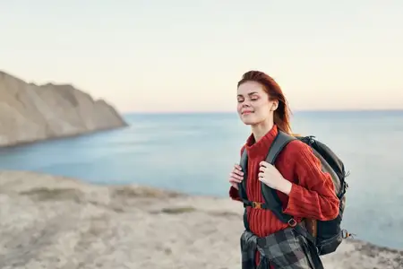 Красивая девушка с рюкзаком в горах, в красном свитере
