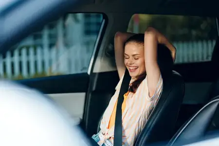 Весёлая молодая женщина сидит в автомобиле, улыбаясь и расслабленно наслаждаясь поездкой