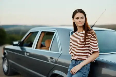 Женщина-водитель возле своего ретро-автомобиля отдыхает после тяжелой дороги и наслаждается пейзажем