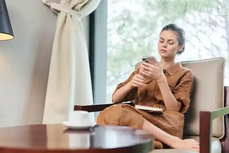 Стильная молодая женщина в коричневом платье, поглощённая своим смартфоном, создаёт безмятежную атмосферу в современном кафе