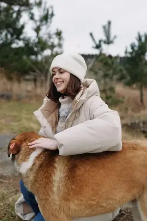 Уличная сцена с модной женщиной в уютном зимнем наряде, обнимающей дружелюбную собаку