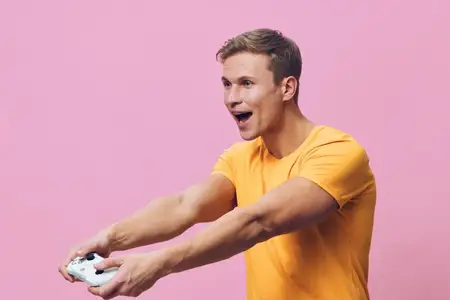 Улыбающийся восторженный мужчина весело играет в видеоигры, держа геймпад обеими руками, выражая радость и волнение