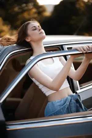 Стильная молодая женщина стоит рядом с винтажным автомобилем, наслаждаясь закатом