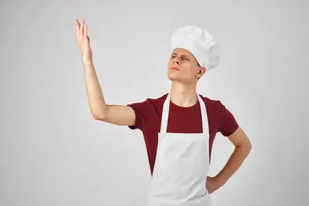 Шеф-повар в фартуке и колпаке на голове, излучающий уверенность в себе, ресторанная профессия