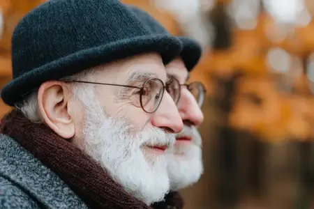 Двое пожилых мужчин улыбаются и наслаждаются временем, проведенным вместе, в живописном осеннем парке в окружении ярких оранжевых листьев