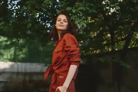 Уличный портрет образа жизни улыбающейся женщины в красном наряде при естественном солнечном свете, передающий уверенность, элегантность и беззаботное настроение в месте на открытом воздухе