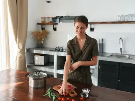 Женщина дома на кухне готовит обед из мяса, овощей и специй на деревянном столе на фоне стильной кухни