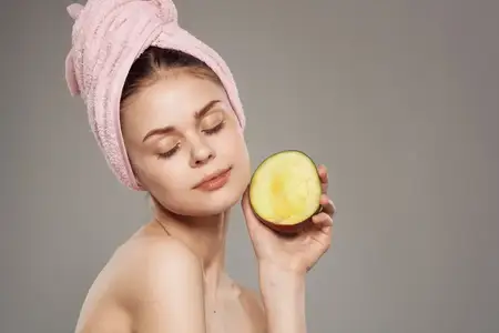 Улыбающаяся женщина с обнаженными плечами, с полотенцем на голове, держит в руке манго