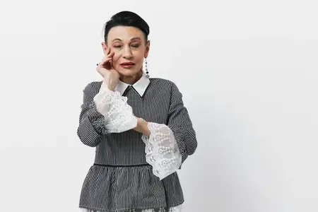 Портрет женщины, прижимающей руку к лицу на фоне белого фона, выражающей эмоции и задумчивость