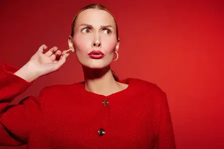 Модная модель в красном наряде и золотых серьгах смотрит в сторону, держа руку возле уха