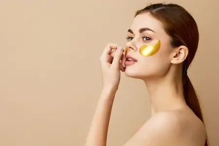 Женщина с золотыми патчами, чистая кожа, улыбается, позирует на бежевом фоне