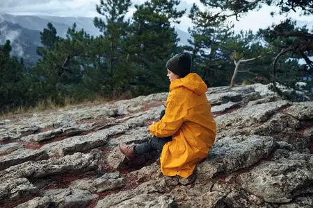 Одинокий путешественник, экипированный для приключений, в ярком желтом дождевике и шляпе, наслаждается захватывающим видом с горной вершины