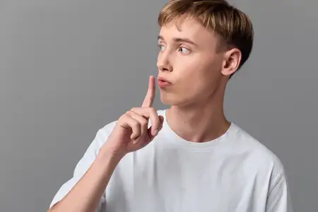 Минималистичное изображение мужчины, призывающего к тишине поднятым пальцем, спокойное выражение на сером фоне, чистая композиция, подходит для редакционных, социальных или маркетинговых тем…