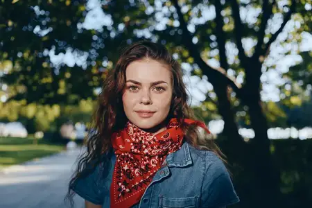 Женщина в стиле лайфстайл, одетая в современный деним в стиле бохо-вестерн с красной банданой, снята в тёплых плёночных цветовых тонах на фоне размытого природного парка