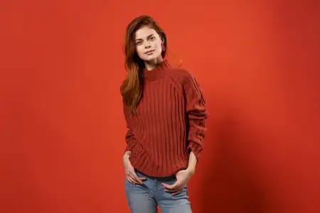 Модная женщина в красном свитере и джинсах, повседневная одежда, позирует на изолированном фоне