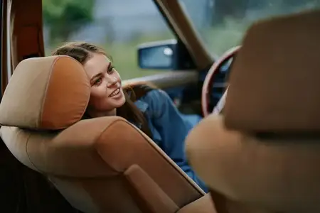 Весёлая молодая женщина отдыхает в винтажной машине с мягким интерьером, излучая счастье и умиротворение, вызывая чувство ностальгии, что идеально подходит для тем путешествий