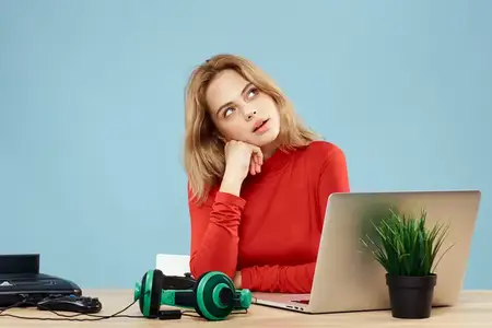 Женщина сидит за столом перед ноутбуком, наушники, контроллер, играет онлайн, образ жизни, синий фон