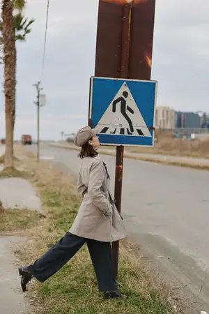 Женщина в повседневной одежде позирует у дорожного знака «пешеходный переход» на обочине в городской местности