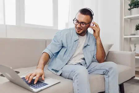Сосредоточенный мужчина работает с ноутбуком, слушая музыку в наушниках, излучая расслабленную, но продуктивную атмосферу