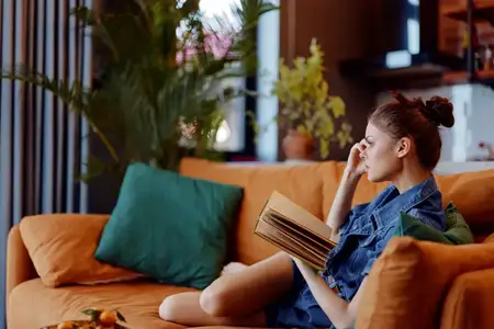 Уютный вечер дома: женщина сидит на диване с книгой и бокалом вина