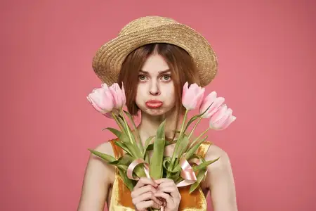 На фотографии запечатлена жизнерадостная женщина в шляпе с букетом цветов, празднующая Международный женский день 8 марта