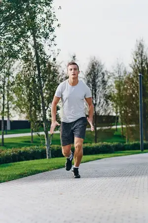 Спортивный мужчина в кроссовках, шортах и футболке бежит в парке на открытом воздухе, занимаясь фитнесом