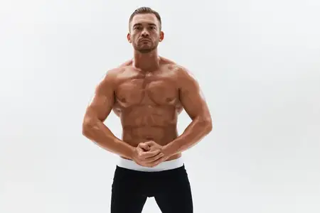 Спортивный мужчина, бодибилдер в трусах, с обнаженным торсом и рельефным прессом, запечатлен в полный рост на фоне
