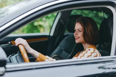 Теплый, непринужденный портрет в салоне автомобиля: расслабленный водитель наслаждается поездкой, естественный свет подчеркивает жизнерадостное выражение лица и руки на руле в комфортной кабине