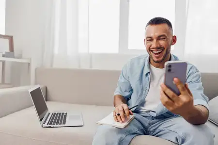 Жизнерадостный мужчина участвует в видео-звонке, демонстрируя яркую атмосферу с естественным светом, заливающим современную гостиную