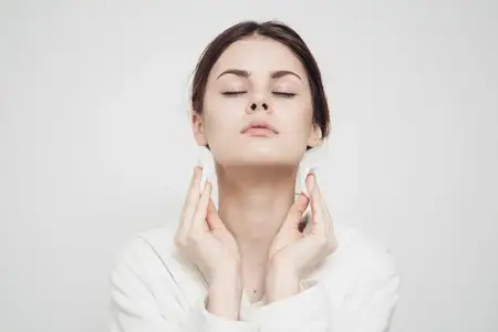 Женщина в светлой одежде вытирает лицо мягкой губкой, чистая кожа, косметология