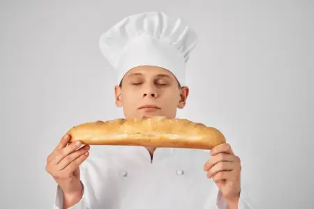 Повар-мужчина держит в руках багет — свежий продукт, профессиональная работа