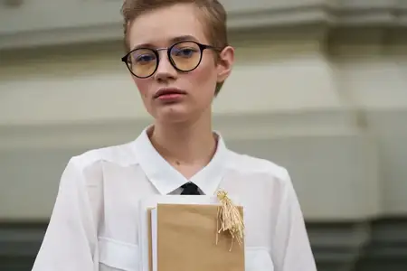 Женщина с короткими волосами держит в руках книгу на открытом воздухе, читая и обучаясь