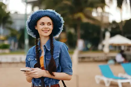 Счастливые молодые женщины наслаждаются летним образом жизни на открытом воздухе: привлекательная девушка с красивой улыбкой пользуется смартфоном в городе